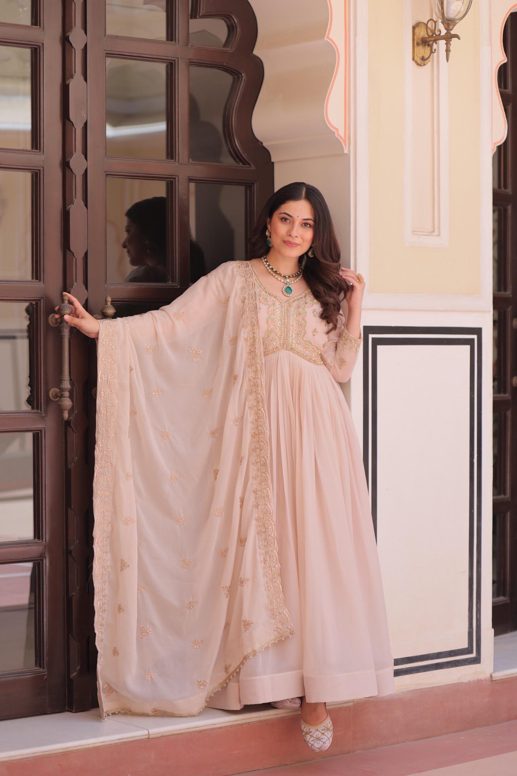 A Woman in a light pink Anarkali gown or dress standing in front of an ornate door.