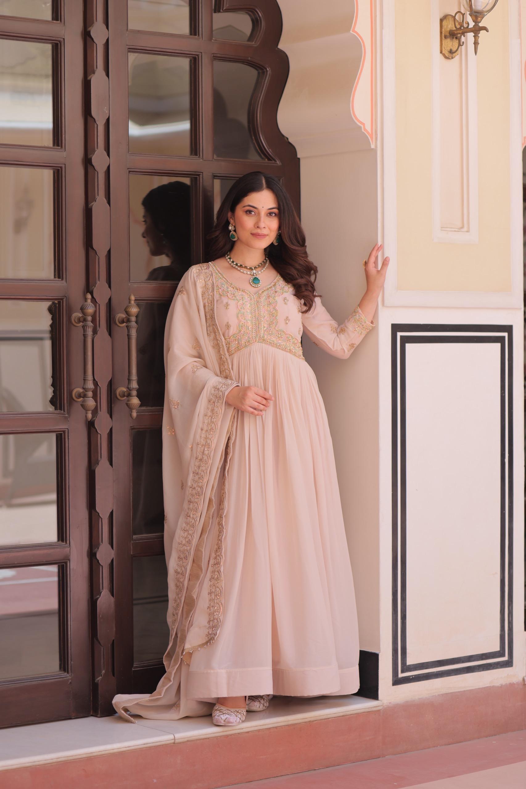 A Woman in a pink Anarkali gown or dress standing in a doorway with decorative elements.