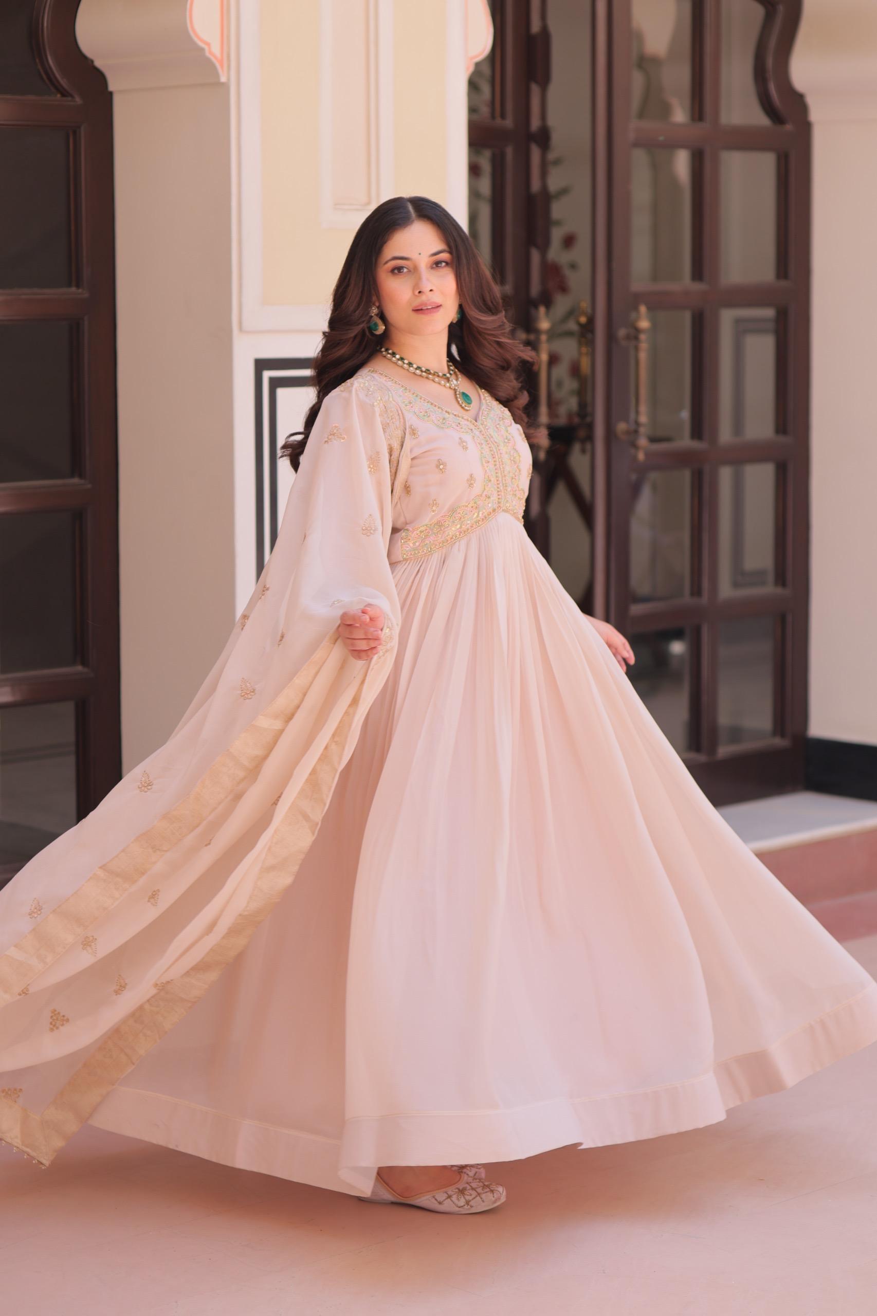 A woman in a pink Anarkali gown or dress standing indoors with decorative elements in the background