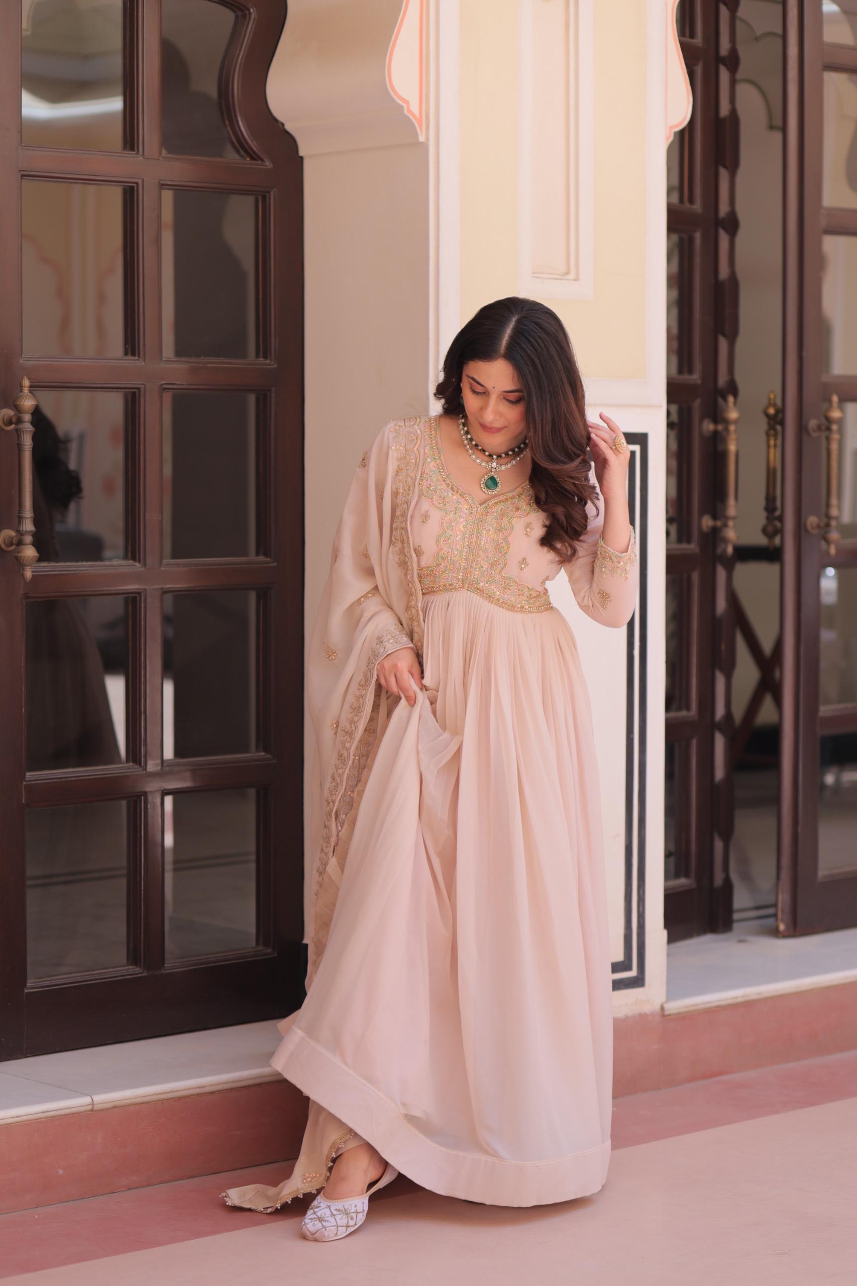 A woman in a pink Anarkali gown or dress standing in a doorway.