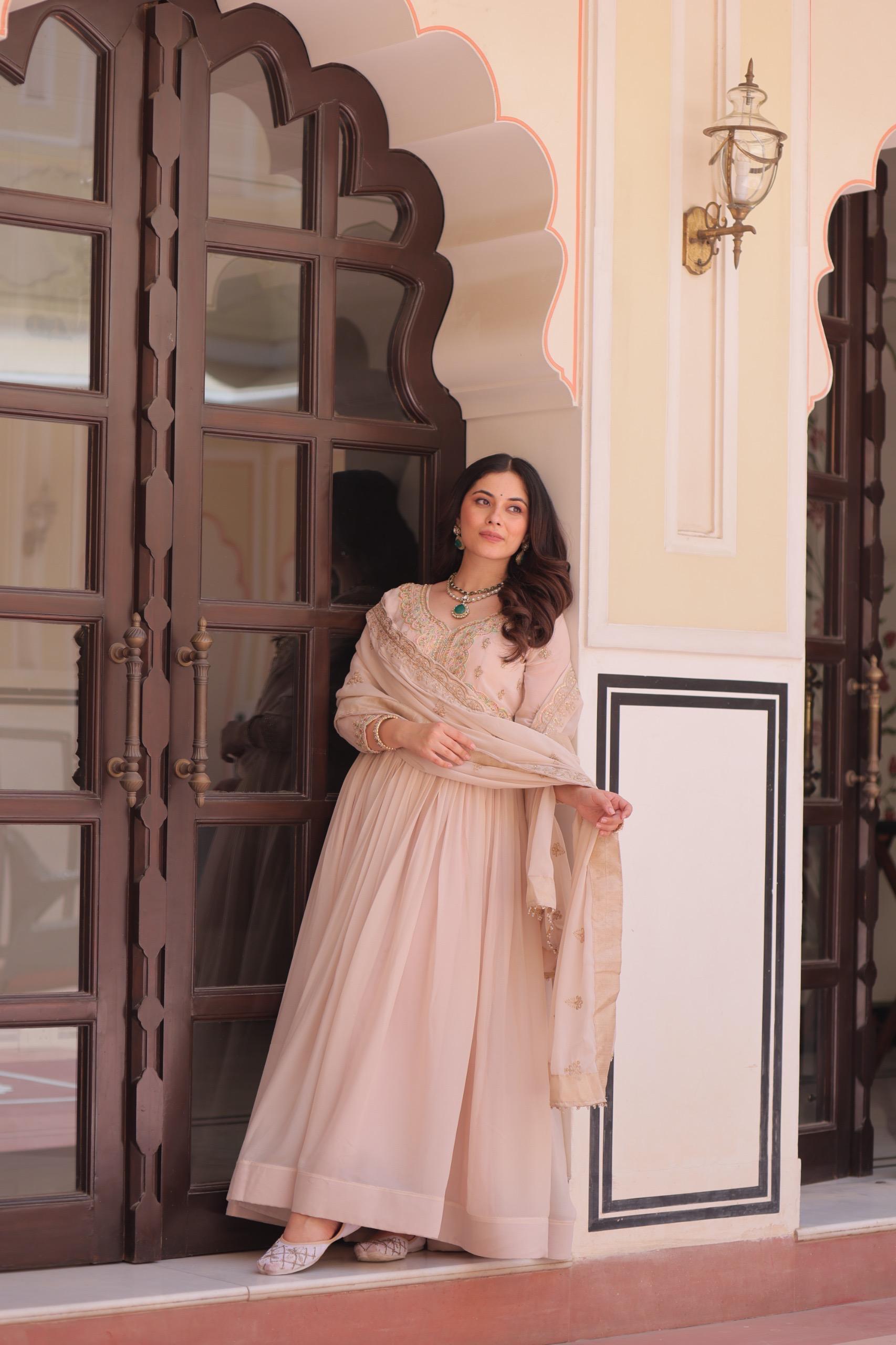 A woman in a pink Anarkali gown or dress standing in front of an ornate door.