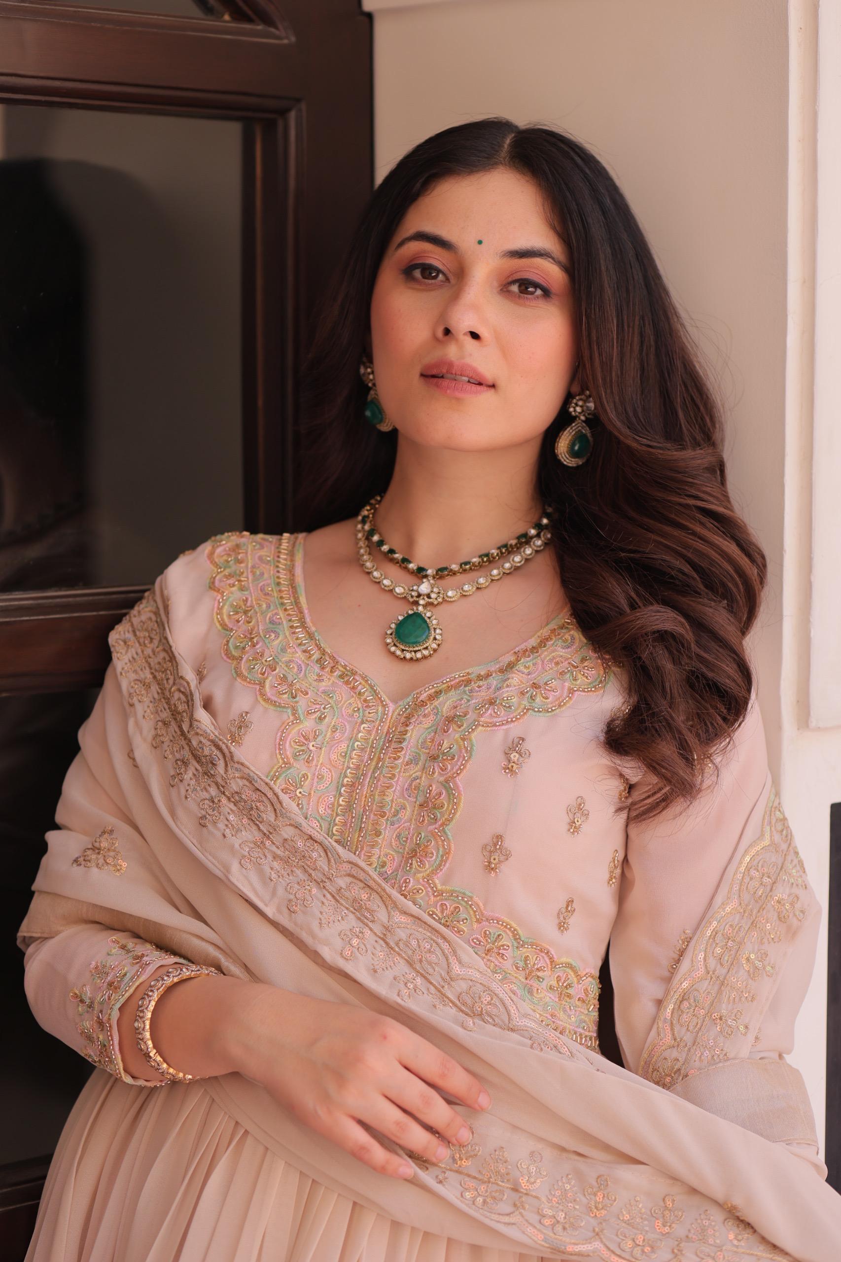 A woman wearing a Anarkali gown or dress with intricate embroidery and jewellery indoors.