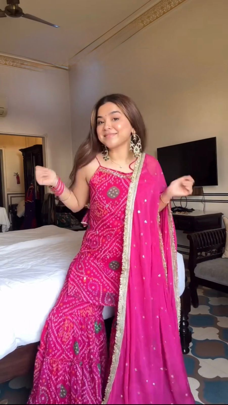 Woman in a pink traditional outfit standing in a room with a bed and television.
