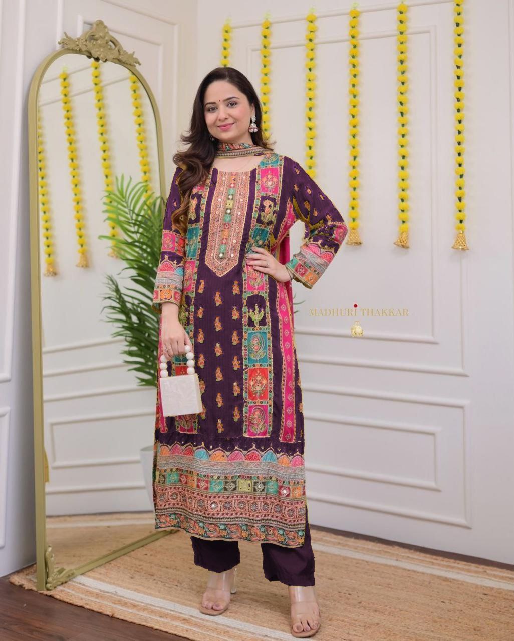Woman in a colorful traditional outfit standing in front of a decorative wall.