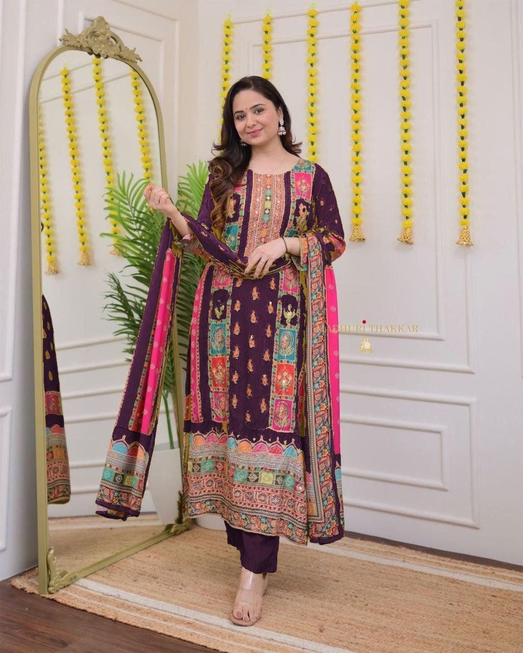 Woman in a patterned outfit standing next to a mirror in a decorated room.