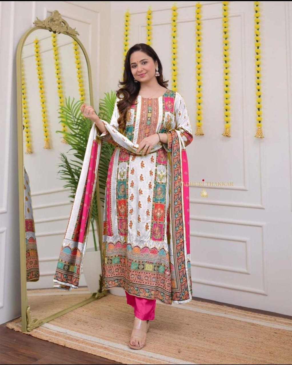 Woman in a colorful traditional outfit standing next to a mirror in a decorated room.