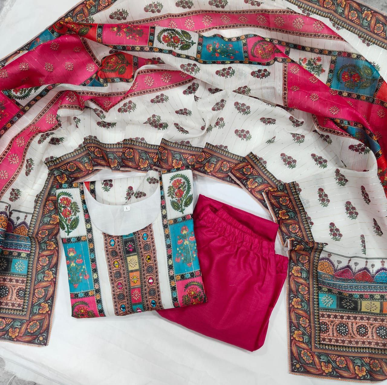 Colorful traditional outfit with a patterned top, white shirt, pink pants, and decorative border on a white background.