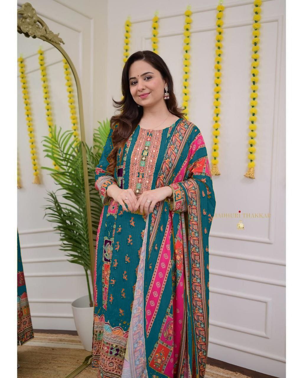Woman in a colorful traditional outfit standing indoors with decorative elements.