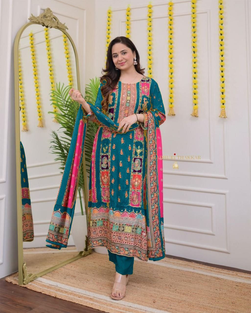 Woman in a colorful traditional outfit standing next to a mirror in a decorated room.